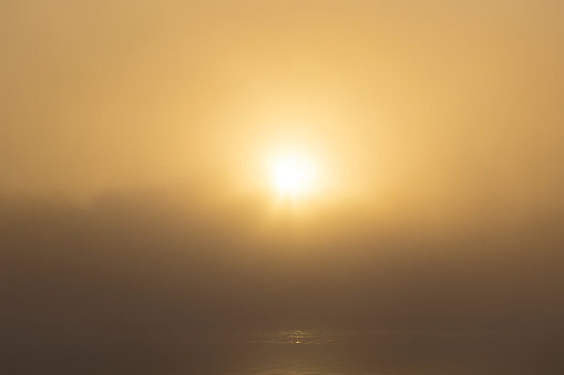 Sun rising above tree silhouette on pond shore with misty fog. Czech landscape background