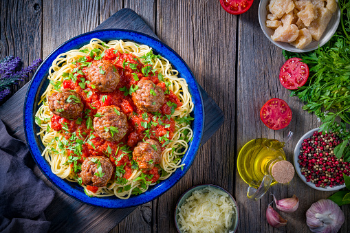 Spaghetti with meat balls and tomato sauce homemade over rustic wooden table board with ingredients, italian food