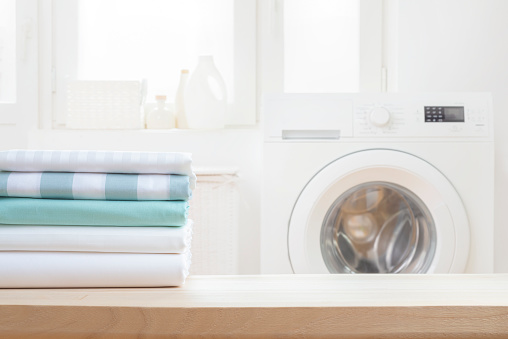 Stack of clean bedsheets on blurred washing machine interior background