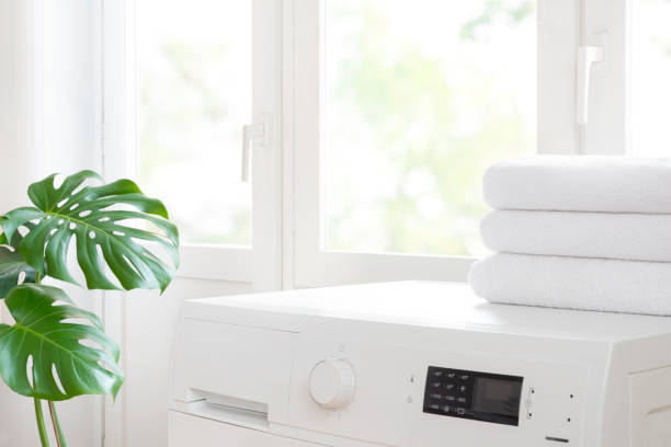 Modern washing machine and clean white towel stack near window stock photo