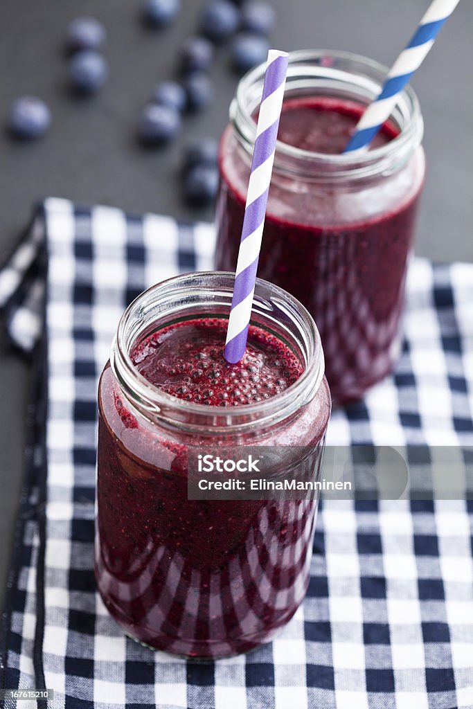 Blueberry smoothies Closeup of two blueberry smoothies in glasses with striped straws resting on checkered napkin with fresh blueberries in background Blueberry Stock Photo