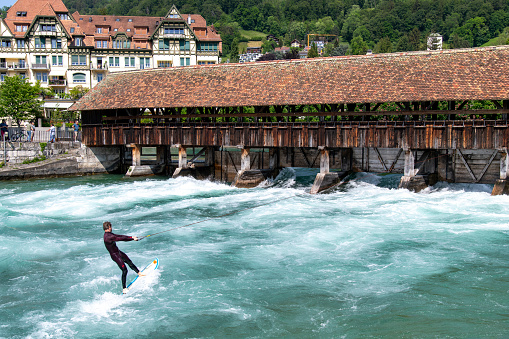 Thun, Switzerland-May 28, 2023; Close view of male surfer on surfboard on waves coming from under the wooden bridge (Flusswelle Thun) crossing the Aare river