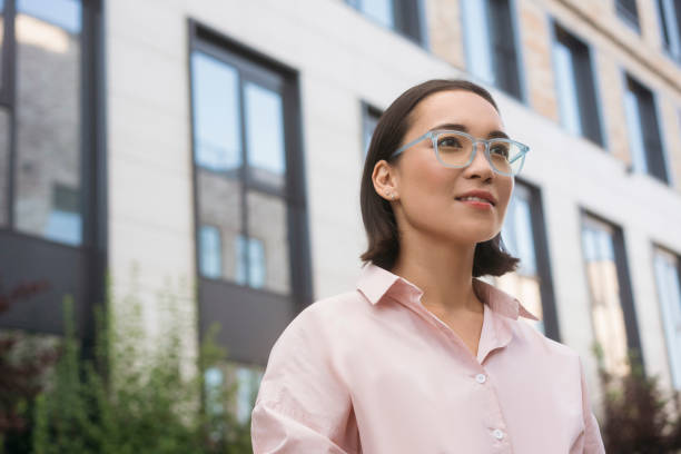 istock Smart smiling asian student wearing stylish eyeglasses standing in university campus, looking away 1676160065