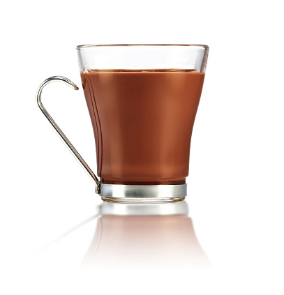 Hot chocolate in a heat-resistant glass with steel handle on a reflective white surface. Authentic studio shot.
