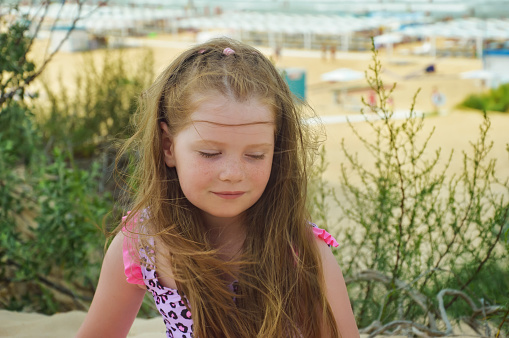 Portrait of a happy girl on the beach. The child plays on the beach near the sea.