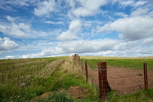 The corner of a wood post and barbed wire fenced field in a hilly agricultural landscape.