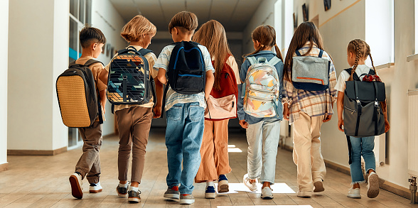 Back to school. A group of schoolchildren with backpacks walk along the school corridor during recess. Education and science concept.