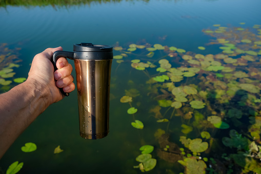 The copper thermos cup or travel mug in the woman's hand. Water background.