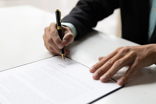 Close up of businessman holding pen signing agreement contract document.