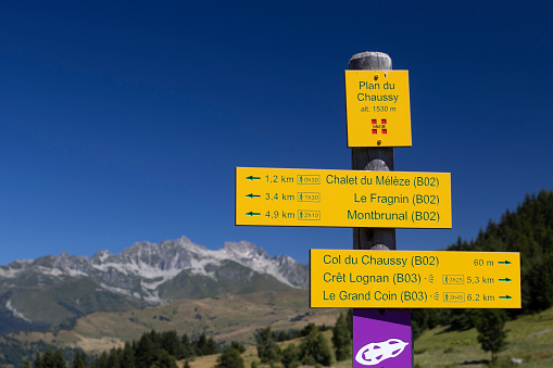 Montvenier, France, 27 July 2023: Trail signpost at Col du Chassy near Montvernier in the French Alps. The area is a popular destination with hikers and cyclists. Mountain background and copyspace.
