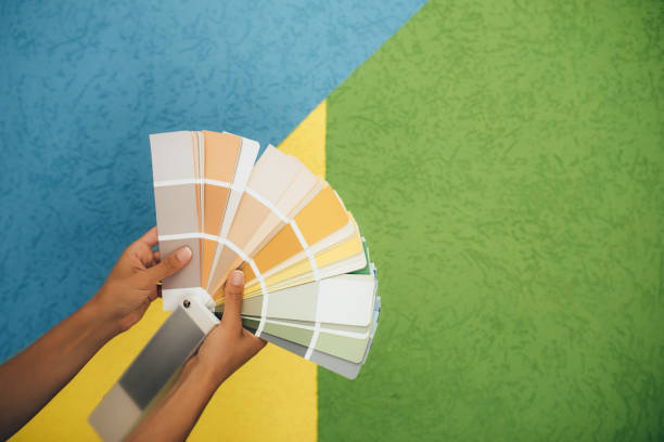 istock Woman choosing color using swatch catalog standing near wall. 1676319036