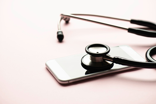 Stethoscope and mobile phone on color background.