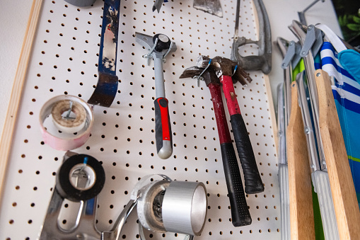 This is a photograph of an assortment of tools hanging on a pegboard in the wall of a garage.