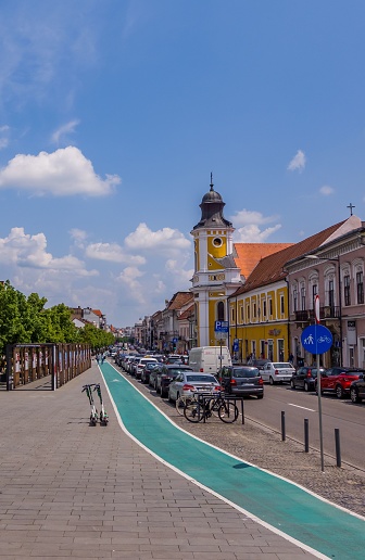 Cluj, Romania – May 27, 2023: A picturesque cityscape of a paved sidewalk flanked by two multi-story buildings on one side and a clock tower on the other
