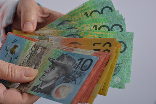 Various denominations of Australian dollars, including $100, $50, $20 and $10 banknotes in a person's hands
