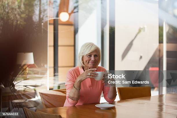 Donna Bere Una Tazza Di Caffè Al Kitchen Table - Fotografie stock e altre immagini di 60-64 anni - 60-64 anni, Abbigliamento casual, Adulto