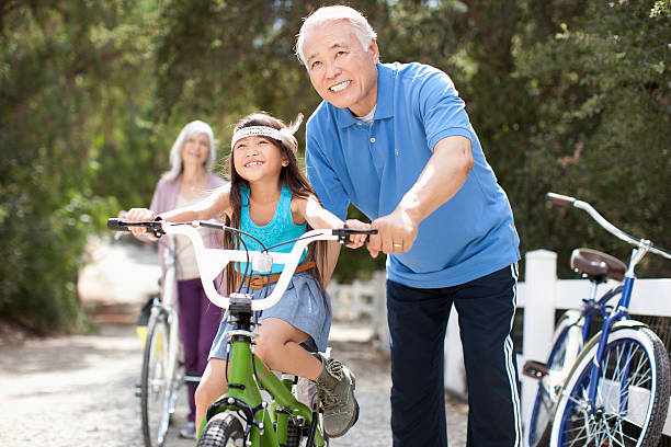 mais homem ajudando neta passeio de bicicleta - family retirement smiling multi generation family - fotografias e filmes do acervo