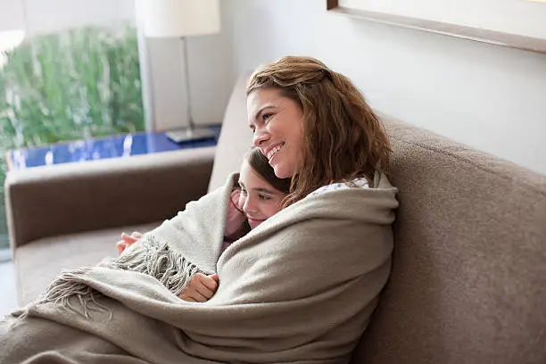 Photo of Mother and daughter wrapped in blanket on couch