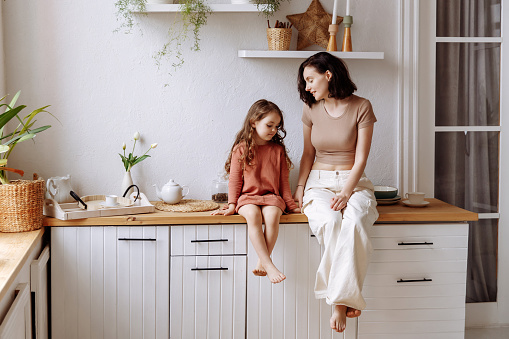 Mom and little daughter in a beautiful stylish kitchen in a modern design look at the copy space. The concept of a catalog or advertisement of furniture or maternity.