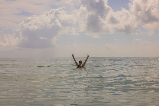 View of woman with hands up in water on pale blue sky background. Atlantic ocean. Miami Beach. USA.