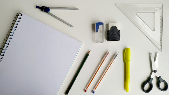 Composition of School Supplies Items on a Simple White Background. White Hardcover Notebook, Pencil, Red and Blue Pens, Eraser, Sharpener, Scissors, Ruler, Compass and Highlighter