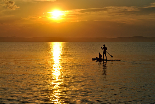 Two lovers are paddleboarding to sunset on Balaton lake in Hungary. Summer vacation water activities.