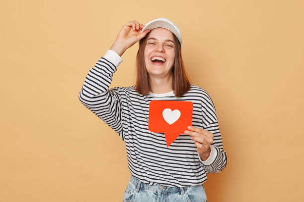 istock Social media content sharing. Notification for recommended content. Counting likes and clicks. woman wearing shirt and baseball cap holding like blogger icon standing isolated  over beige background 1676495002
