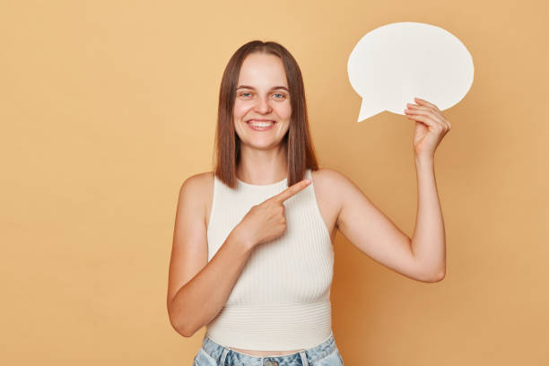 istock Creative ideas in an imaginative mind. Blank space for your own opinion. Cheerful brown haired woman wearing casual clothing holding empty bubble speech cloud standing isolated over beige background 1676495564