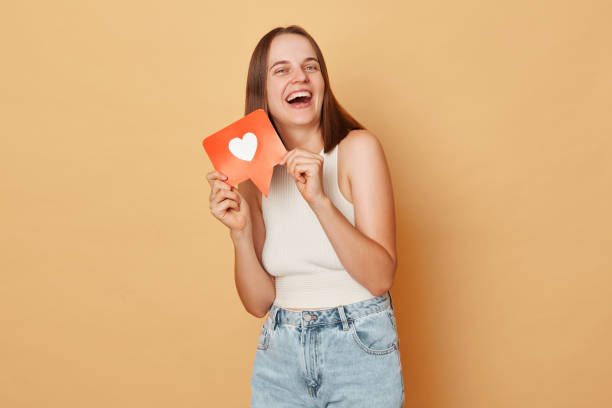 istock Blog communication. Blogger network. Web communication. Like counter. Laughing brown haired young woman wearing casual clothing holding red like icon standing isolated over beige background 1676495581