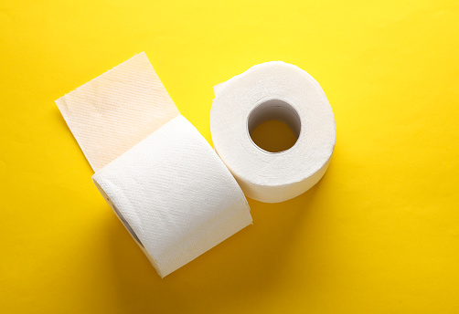 Two rolls of white toilet paper on yellow background with a shadow