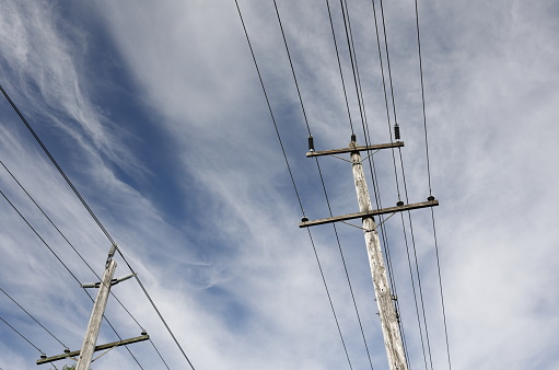 Low angle view of wooden poles with power lines in Metro Vancouver, British Columbia. Cloudy morning in early summer.