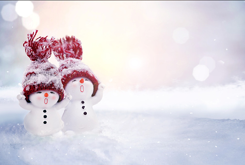 Two little snowmen in caps on snow in the winter. Festive background with a funny snowman. Christmas card, copy space.