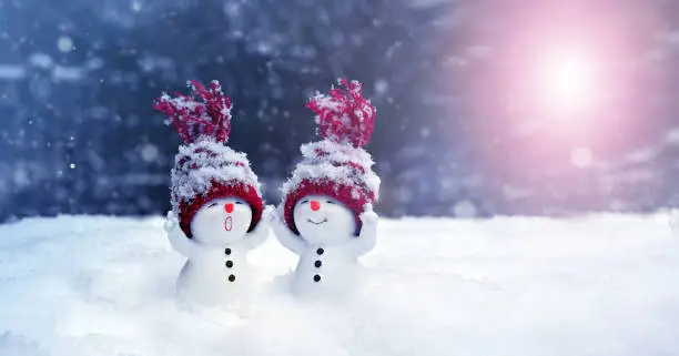 Photo of Two little snowmen in caps on snow in the winter. Background with a funny snowman. Christmas card.