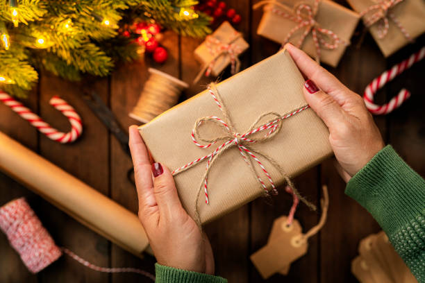 istock Woman's hands holding a Christmas present wrapped with brown paper. 1676541292