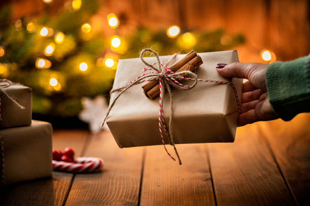 istock Woman's hands holding a present near the Christmas tree. 1676541294