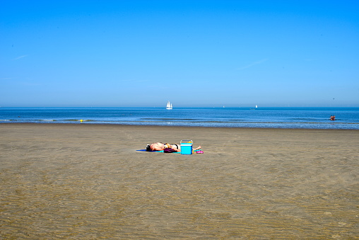 Blankenberge, West-Flanders, Belgium September 7, 2023: white couple laying on the beach enjoying sunbathing on a sunny day in September in front of the sea with a sailing ship in background