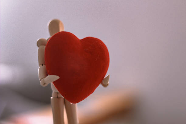 Wooden mannequin toy holding red heart in hands with copy text space illustrating valentine day and other romantic gifts.