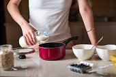 Woman adding milk while making morning breakfast oatmeal cereals in the kitchen at home