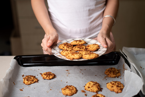 Woman arranging fresh homemade coconut cookies on a plate in the kitchen at home closeup