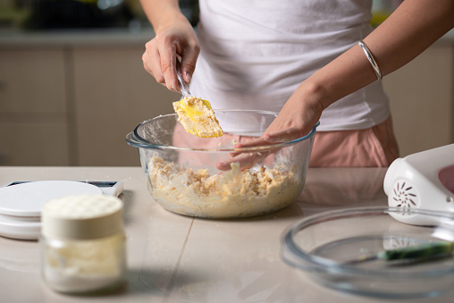 Woman mixing ingredients for coconut cookies dough of sugar, beaten eggs, butter and flour for making homemade desserts in the kitchen at home closeup