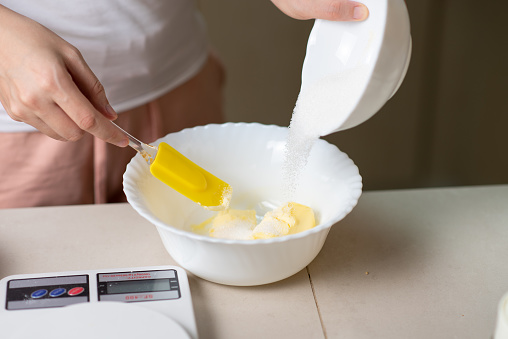 Woman mixing ingredients for dough of sugar, beaten eggs, butter and flour while making cookies in the kitchen at home closeup