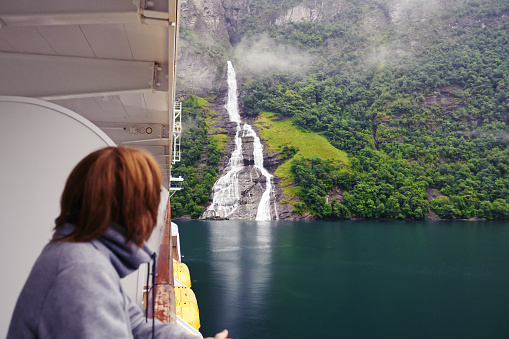 Woman on a cruise ship looking at the 'Suitor Waterfall' or 'Bottle waterfall' which  lies opposite the more famous seven sisters located along the Geirangerfjorden in Norway