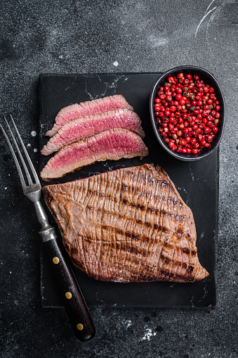 Grilled Flank Steak BBQ on a marble board. Black background. Top view.