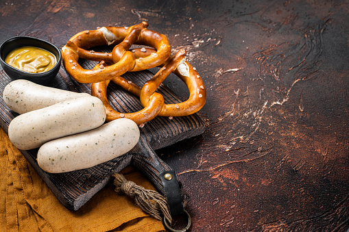 Traditional German pretzel with white sausage and mustard. Dark background. Top view. Copy space.