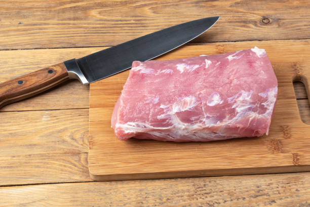 istock Raw pork meat on a wooden cutting board and a kitchen knife. 1676648449