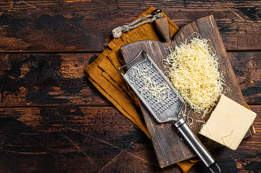 Piece of semi hard cheese and grated cheese with grater. Wooden background. Top view. copy space.