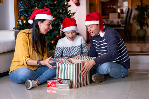 Happy couple and their son opening a gift together looking very excited and surprised during their Christmas celebration - Holiday celebration concepts