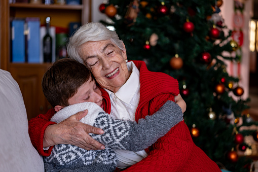 Loving grandson and grandmother hugging with eyes closed while celebrating Christmas at home - Family and holidays concepts