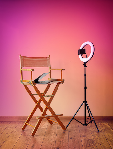 Director's chair, ring lights, digital camera with laptop and hats on colorful background with recording equipment