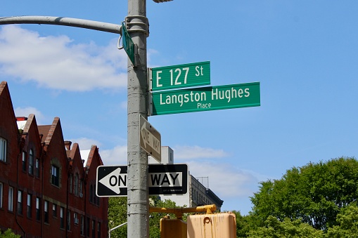 Looking up view of the green New York City street signs for E 127th St aka Langston Hughes Place on the corner of 5th Avenue near the poet's old brownstone in Harlem, New York